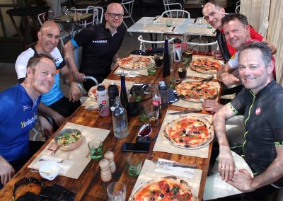 Male cyclists smiling whilst eating pizza